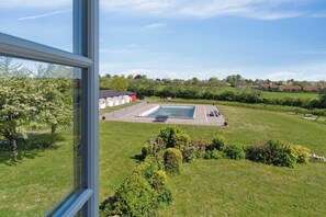 A swimming pool with a surrounding deck, a grassy area, and a view of houses in the distance.