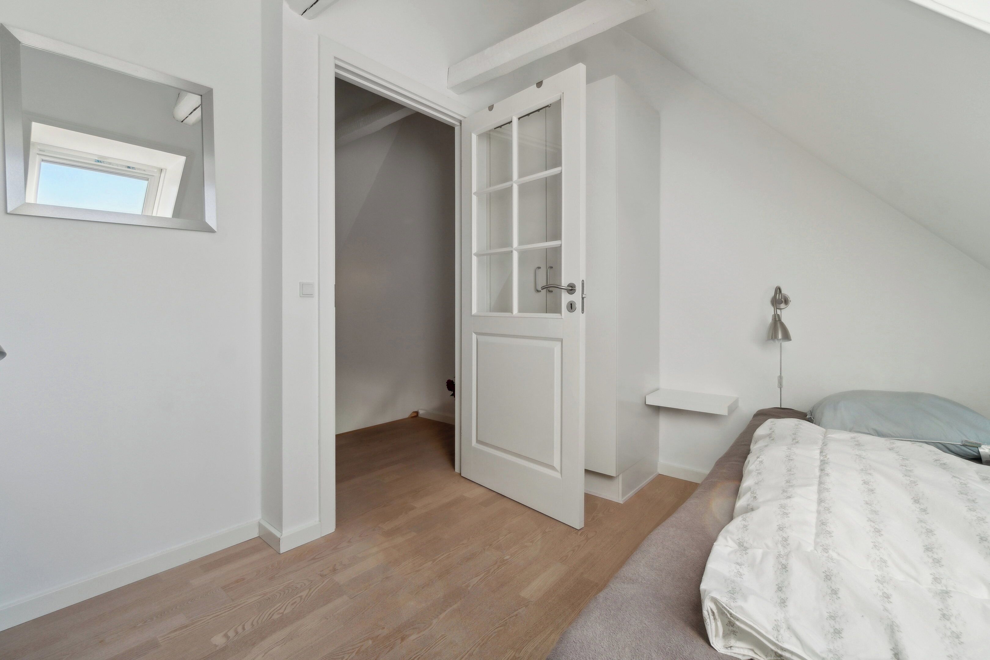 Een slaapkamer met een schuine plafond, een bed met een beddegoed met een patroon, een nachtkastje en een bijzettafeltje.