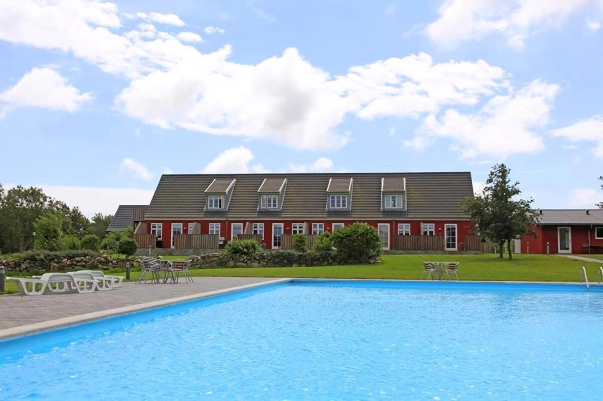 Ein Schwimmbecken mit Liegestühlen und ein Gebäude mit schrägem Dach im Hintergrund.