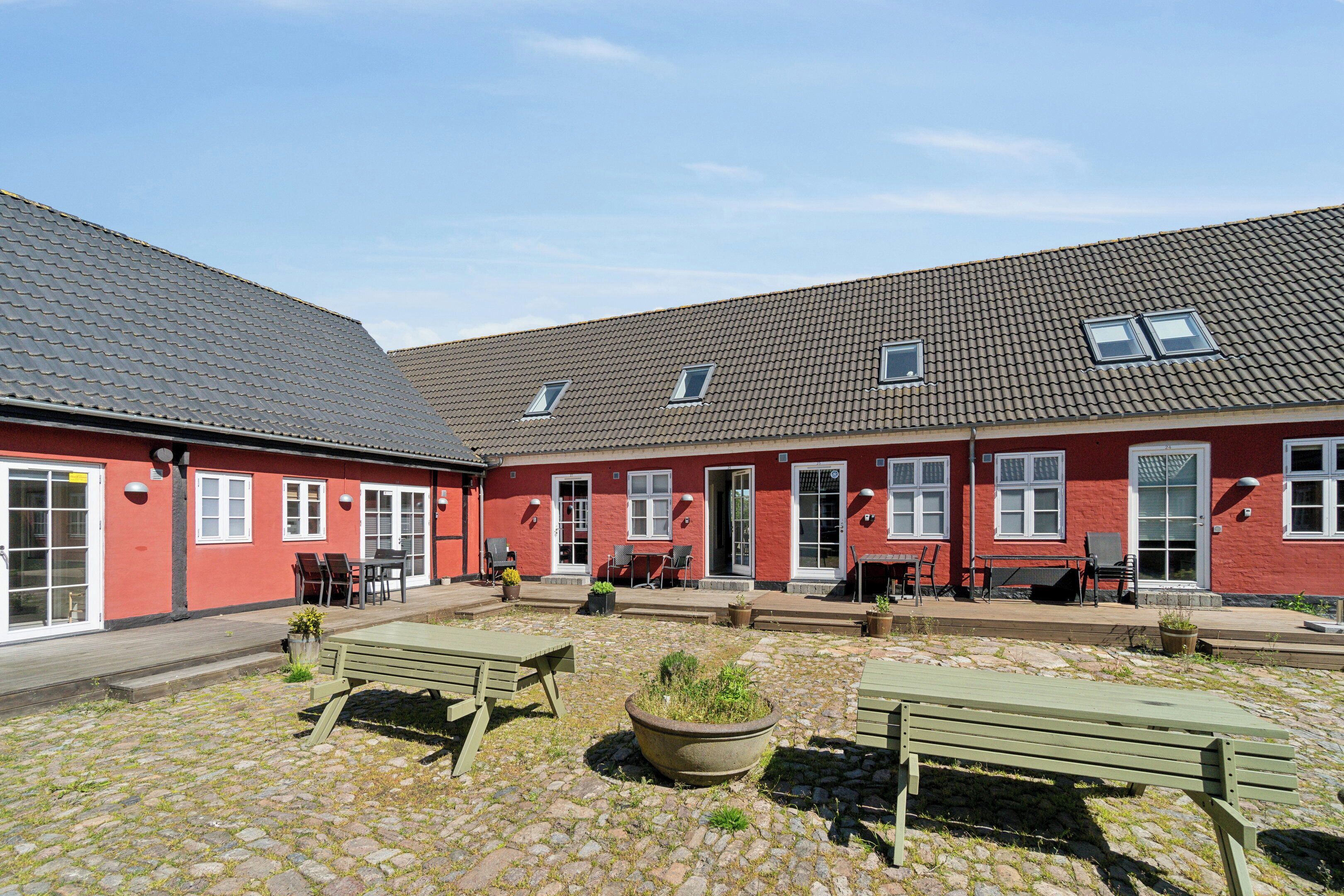 Een rood gebouw met een pannendak, terras en een kinderafsluiting van cobblestones.