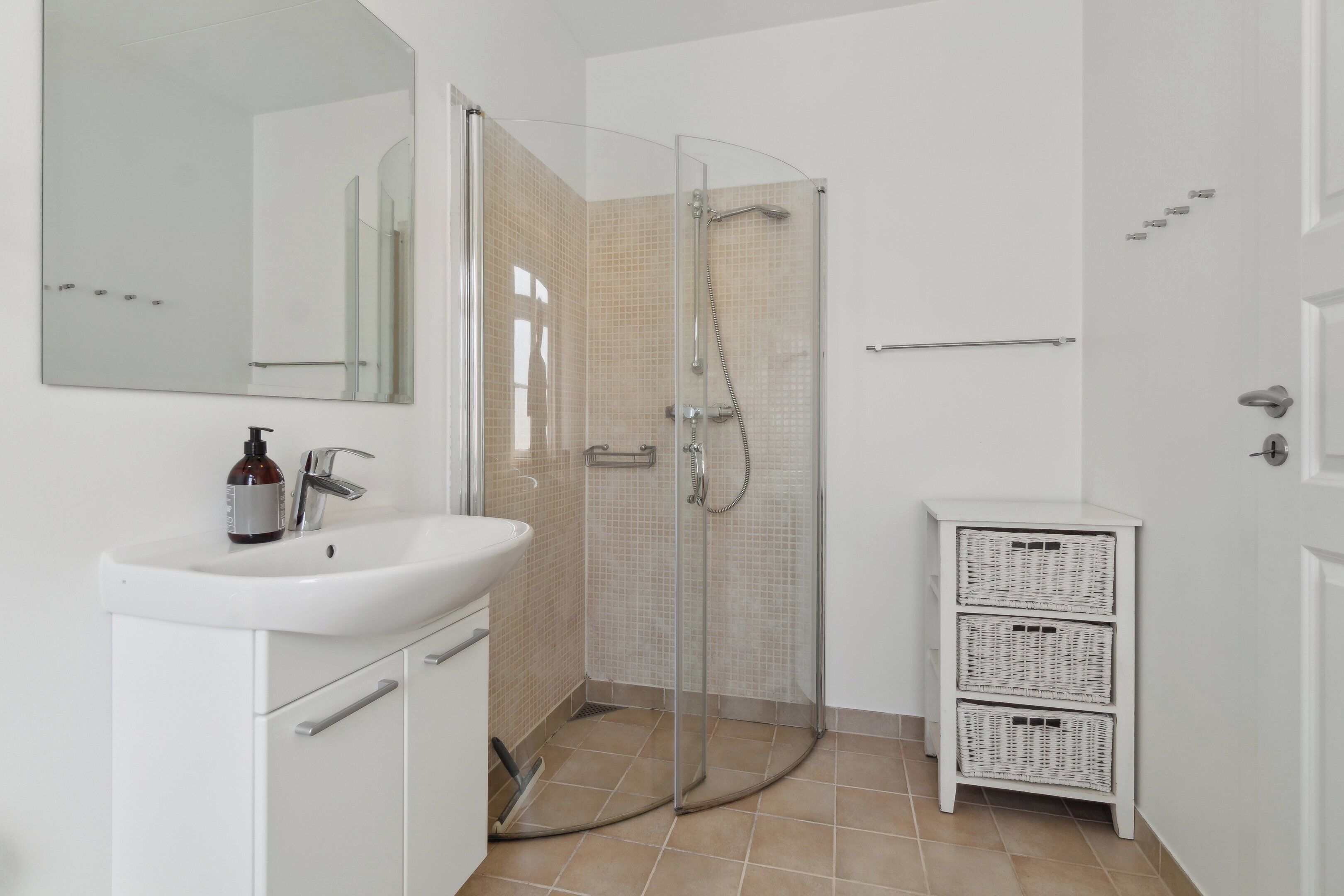 Une salle de bain avec une douche à parois de verre, un lavabo blanc, un miroir et un meuble blanc.