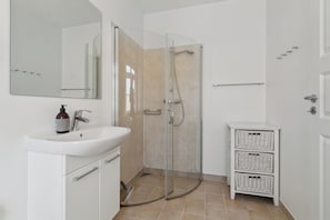 A bathroom with a glass-enclosed shower, a white sink, a mirror, and a white cabinet.