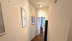 A hallway with framed artwork on the walls, a wooden floor, and a door leading to another room. - Studio Apartment 'Panorama' with Wi-Fi (Lingen (Ems))