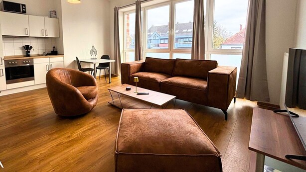 A modern living room with a brown sofa, a brown chair, a wooden coffee table, and a TV on a wooden stand. - Studio Apartment 'Panorama' with Wi-Fi (Lingen (Ems))