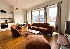 A modern living room with a brown sofa, a brown chair, a wooden coffee table, and a TV on a wooden stand. - Studio Apartment 'Panorama' with Wi-Fi (Lingen (Ems))