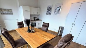A dining area with a wooden table, four chairs, a vase, and a trash can. - Studio Apartment 'Panorama' with Wi-Fi (Lingen (Ems))