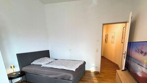 A bedroom with a bed, a bedside table, a lamp, a TV, and a hallway leading to another room. - Studio Apartment 'Panorama' with Wi-Fi (Lingen (Ems))