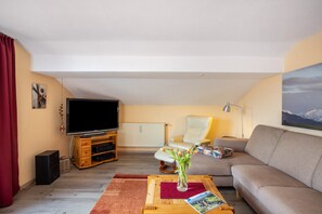 Een woonkamer met een televisie, bank en een bijzettafel met een bloevas.
