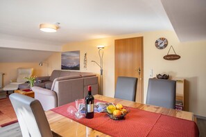 Een eethoek met een houten tafel, stoelen, een fles wijn en een mand met fruit.