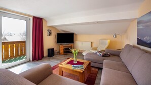 Una sala de estar con un sofá, una mesa de centro con una revista, un televisor y un ventanal con vistas.