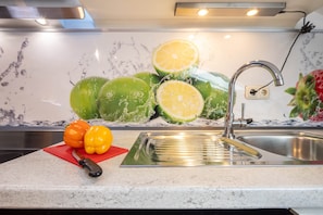A kitchen with a stainless steel sink, a red cutting board, and a knife.