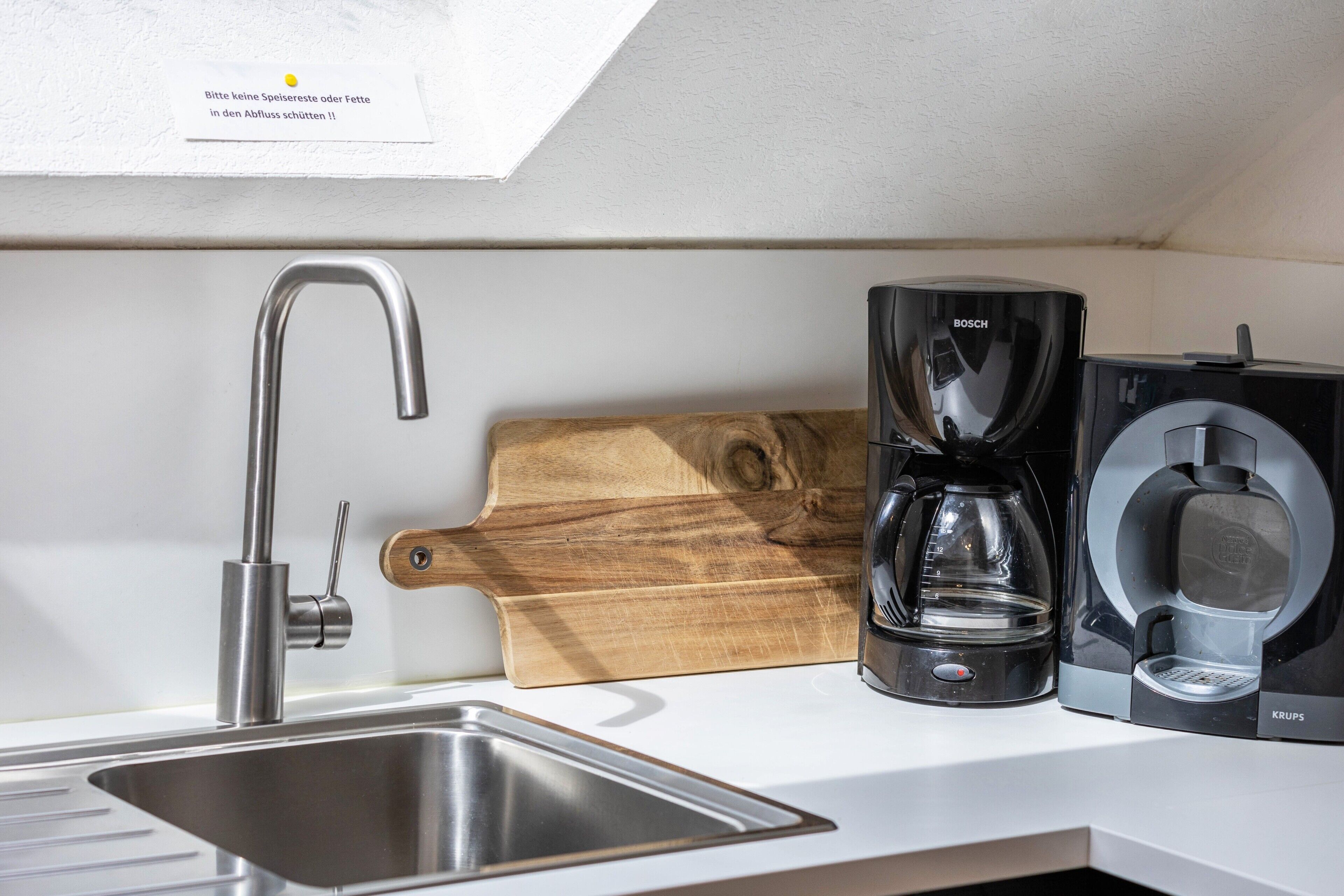 A kitchen with a stainless steel sink, a Bosch coffee maker, and a Krups coffee machine.