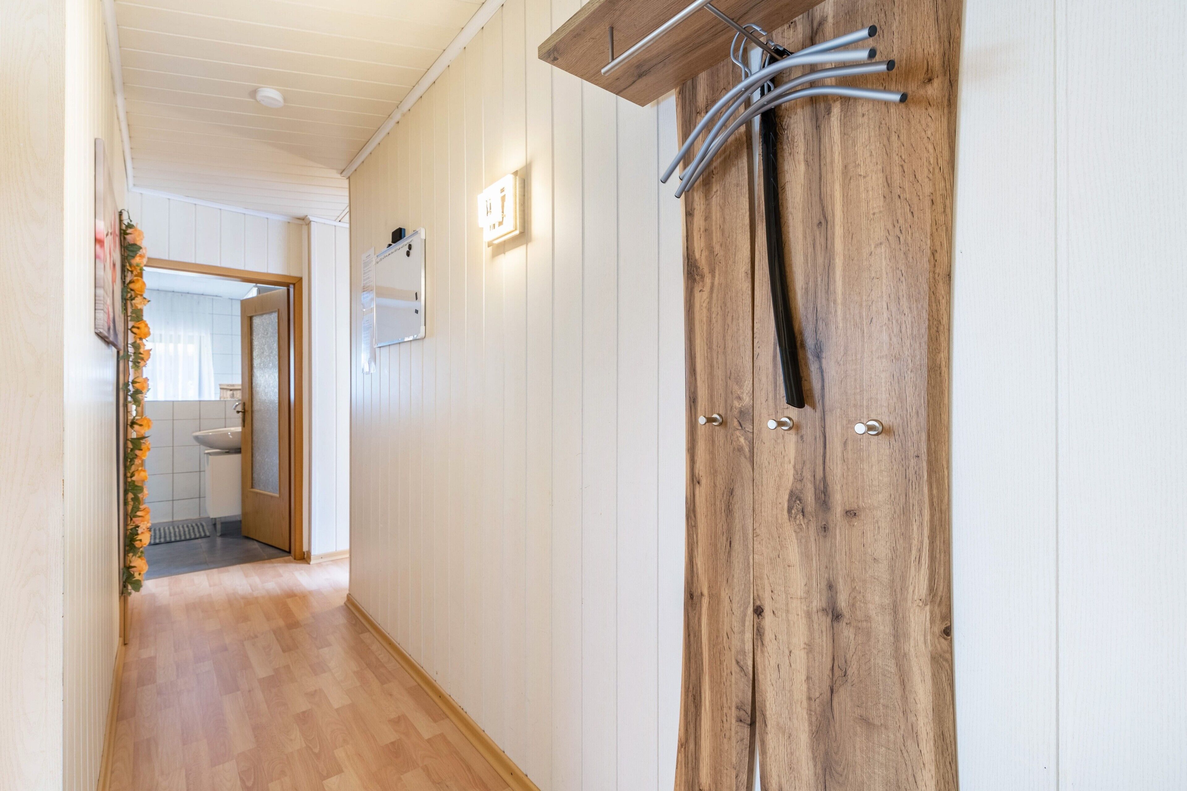 Un corridoio con pavimento in legno, una porta in legno dotata di maniglie metalliche e un interruttore a parete.