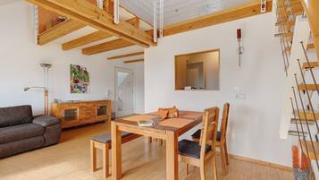 Een ruime woonruimte met een houten eettafel, stoelen, een bank, een kast en een trap.