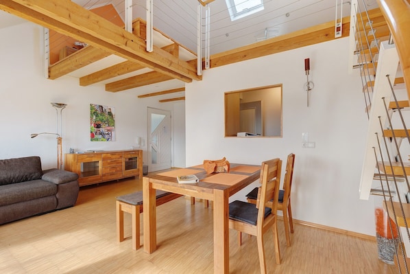 A spacious living area with a wooden dining table, chairs, a sofa, a cabinet, and a staircase.