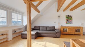 Un espai tipus loft amb sostre de fusta, un sofà modular, una taula de dinar de fusta i un armari.