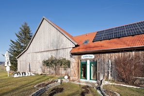 A wooden building with a green door labeled 'Birkethofstadel,' a solar panel on the roof, and a chessboard outside.