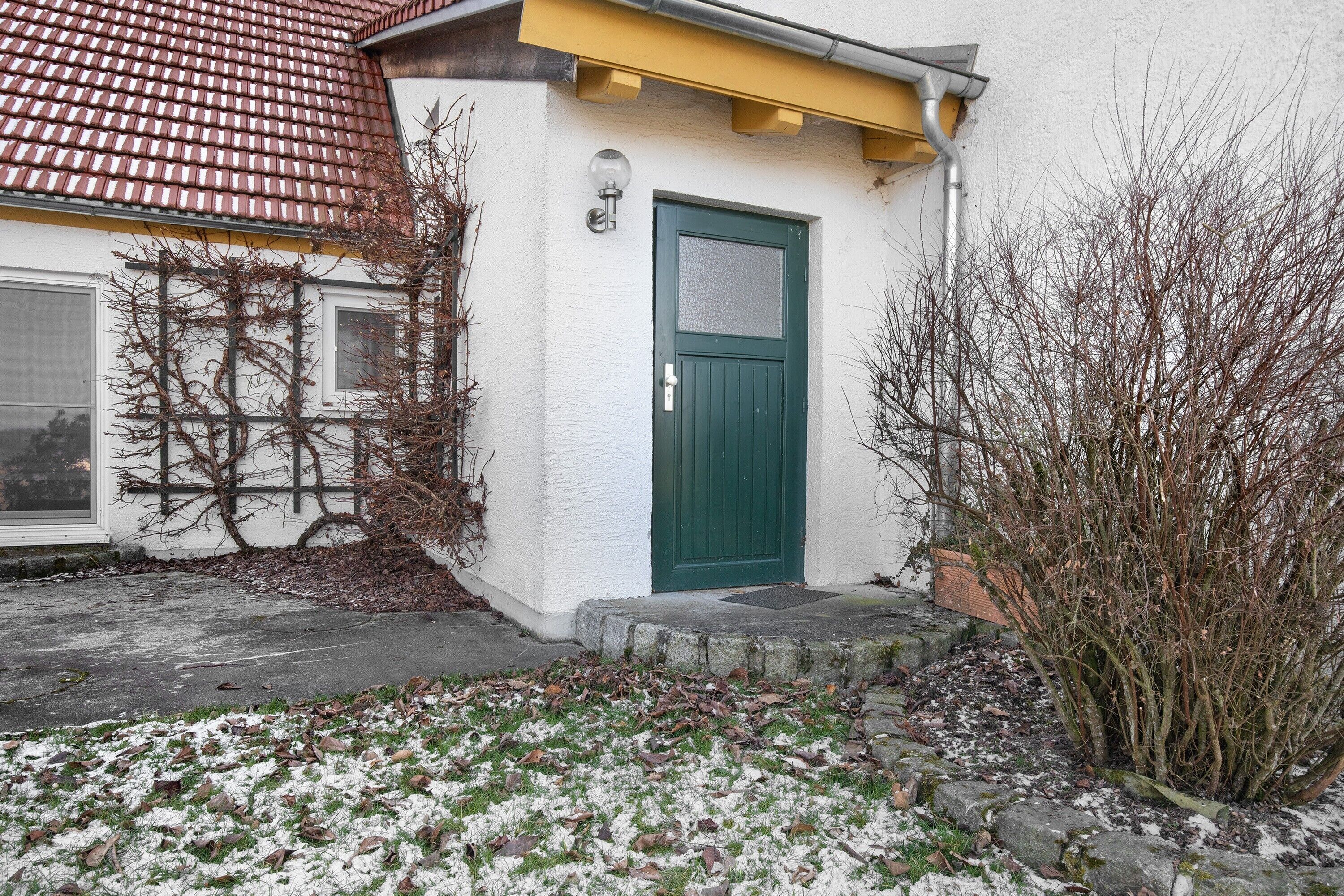 A house with a green door, a white exterior, and a red-tiled roof.