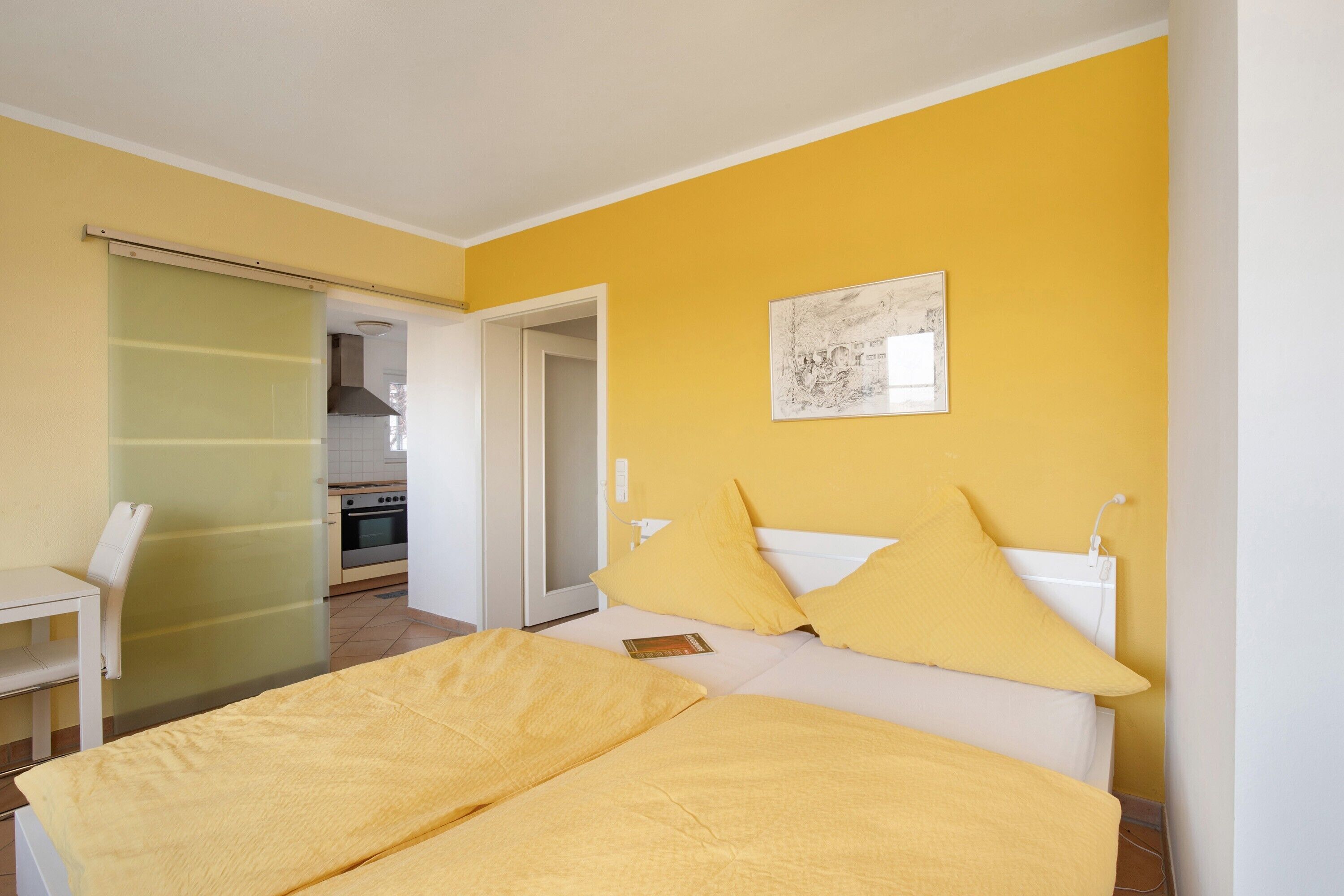 Um quarto com uma cama, uma cadeira, uma mesinha de cabeceira e um quadro na parede.
