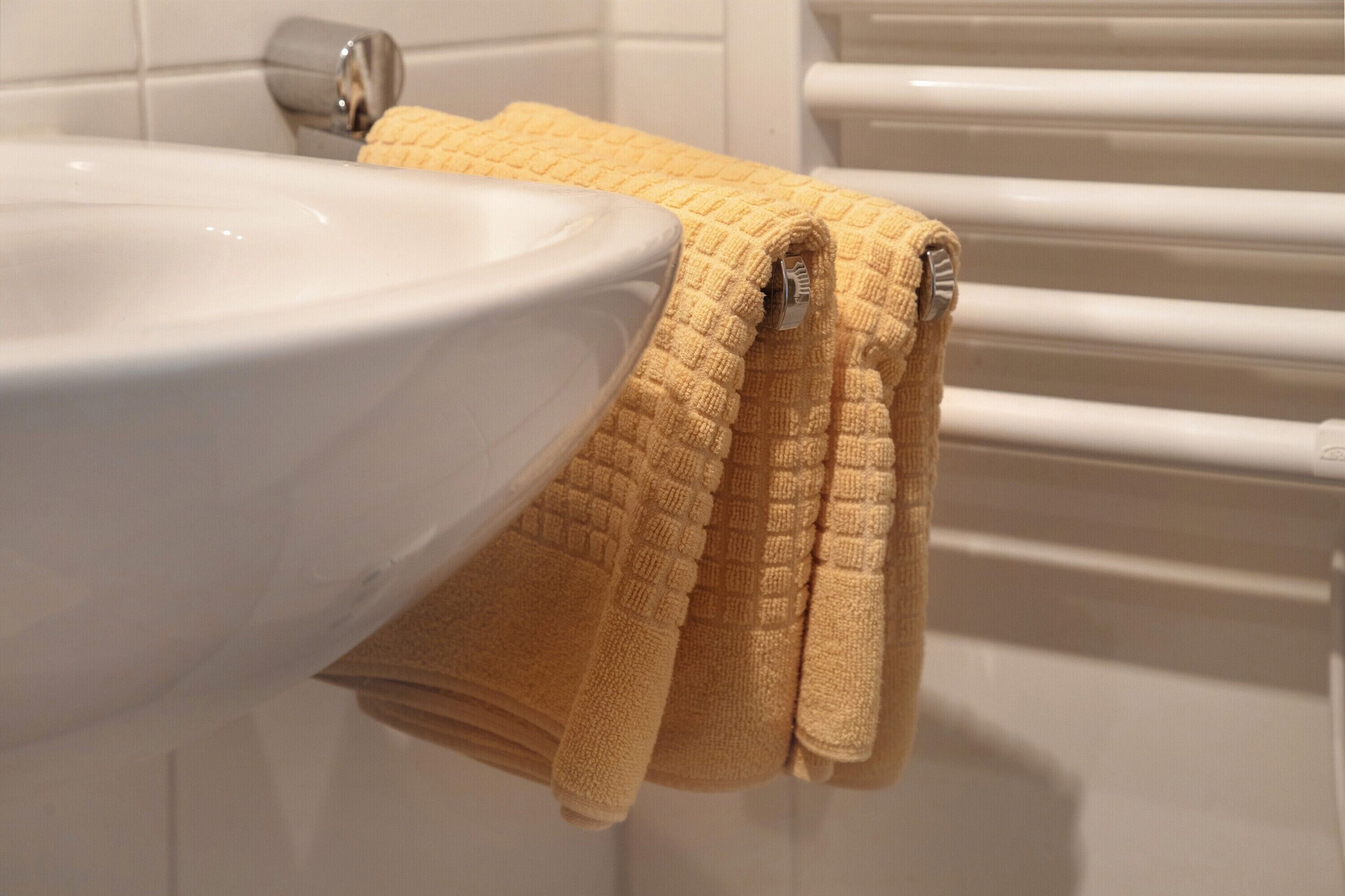 Une salle de bain avec un lavabo blanc, une serviette jaune et un porte-serviettes blanc.