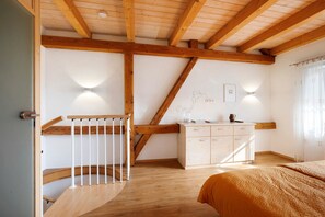 A bedroom with a wooden staircase, a bed, a bedside table, a dresser, and a wall-mounted light fixture. - Apartment 'Birkethof - Fernblick' with Mountain View, Private Terrace and Wi-Fi (Grimoldsried)