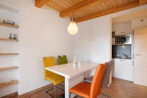 A compact kitchen with a white table, orange and yellow chairs, and a hanging light bulb. - Apartment 'Birkethof - Fernblick' with Mountain View, Private Terrace and Wi-Fi (Grimoldsried)
