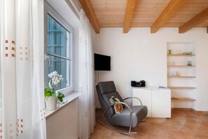 Une pièce avec une fenêtre, une chaise, un téléviseur et un meuble.