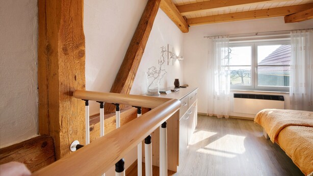 Ein Zimmer mit einer Holztreppe, einem Bett, einem Fenster mit Vorhängen und einer Heizung.