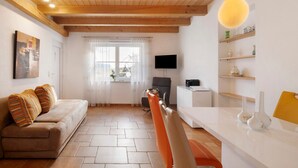 Ein Wohnzimmer mit einer Couch, einem Esstisch, einem Fernseher und einer Küchenzeile.