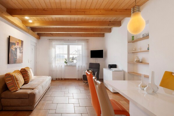A living room with a sofa, a dining table, a TV, and a kitchen area. - Apartment 'Birkethof - Fernblick' with Mountain View, Private Terrace and Wi-Fi (Grimoldsried)
