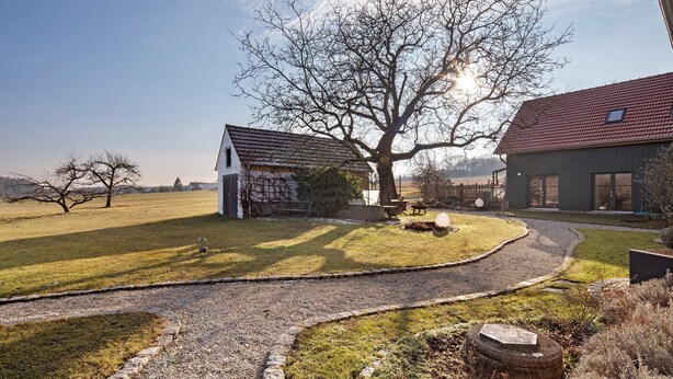 Ein ländliches Anwesen mit einem Schotterweg, einem Steinhaus und einem großen Baum.