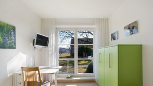 Ein Zimmer mit Esstisch, einem an der Wand montierten Fernseher, einem grünen Schrank und einem Fenster mit Blick ins Freie.