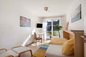 A bedroom with a bed, a desk, a chair, a TV, and a window with curtains.