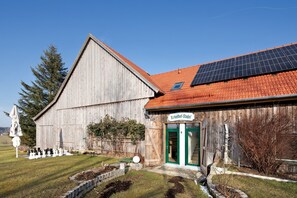 A wooden building with a green door labeled 'Birkethofstadel,' a solar panel on the roof, and a chessboard outside.