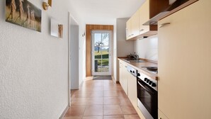 A narrow kitchen with a view through the door, wooden cabinets, and a stove. - Apartment 'Birkethof Teichblick' with Mountain View, Private Terrace, and Wi-Fi (Grimoldsried)