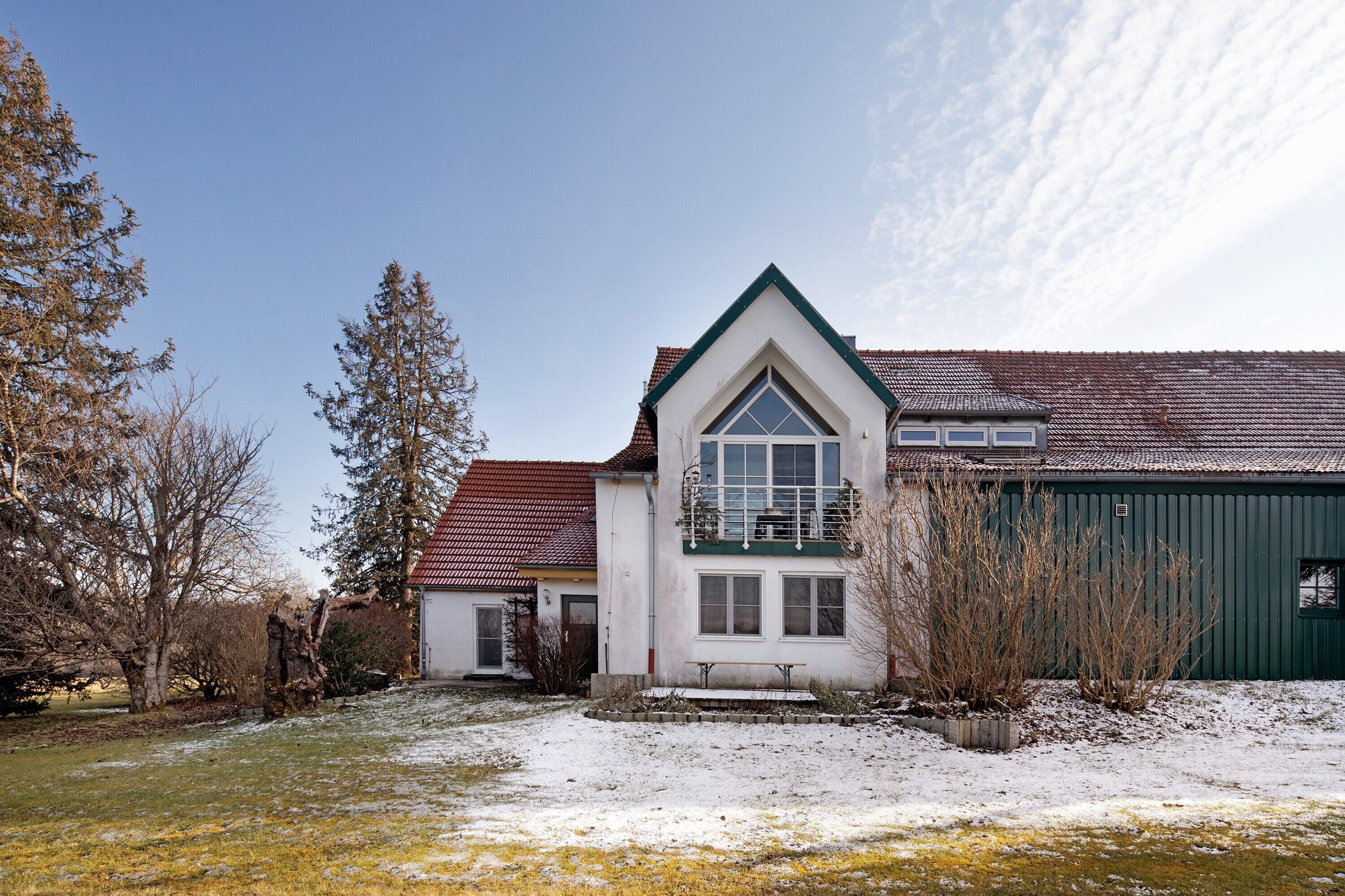 A two-story house with a triangular roof, a green garage, and a snow-covered yard.