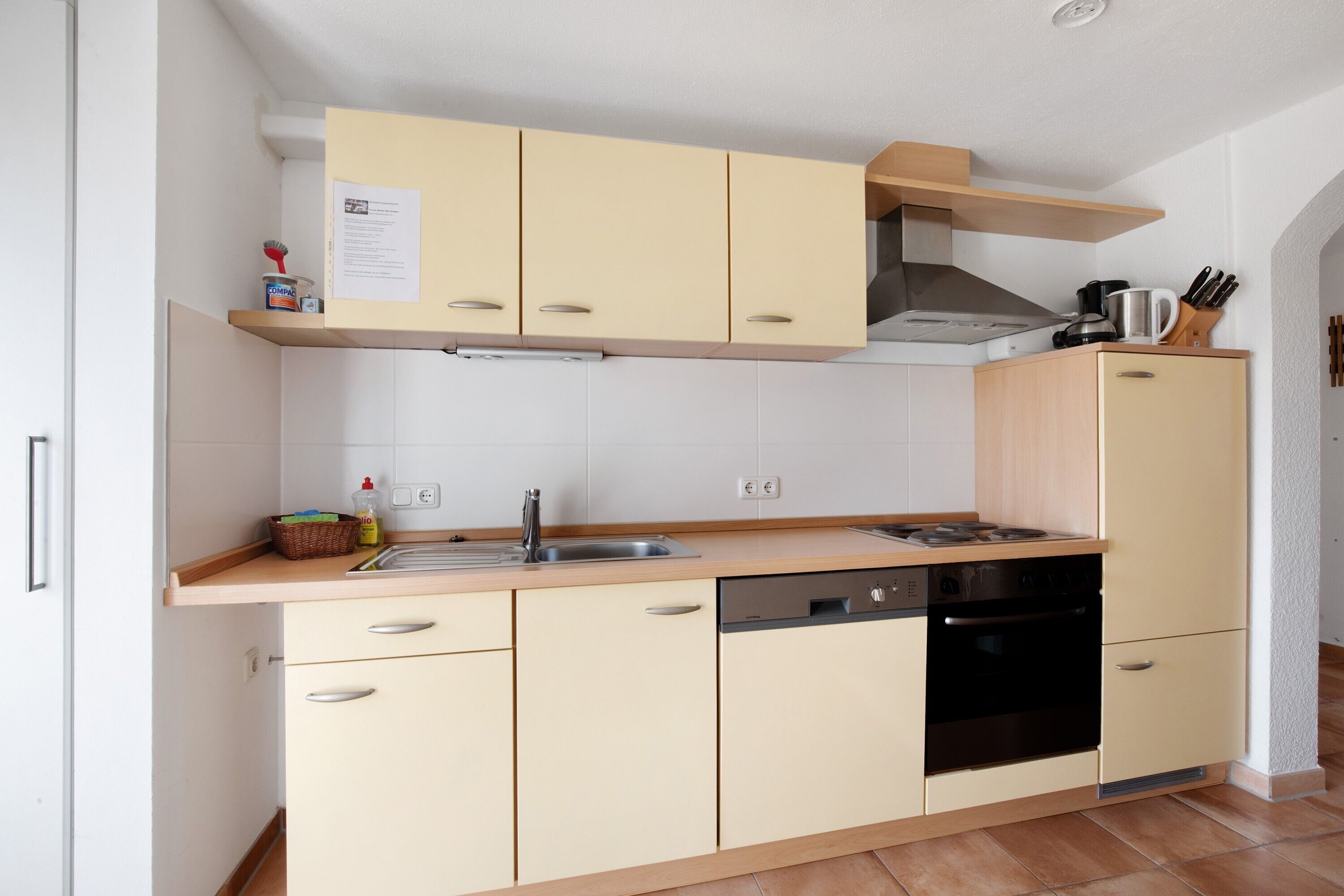 A compact kitchen with a dishwasher, stove, and a small cabinet with a paper on top.