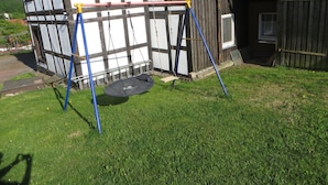 A swing set in a grassy yard with a wooden house in the background.