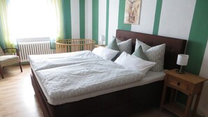 A double bed with white bedding, a nightstand with a lamp, a wooden chair, and a radiator.