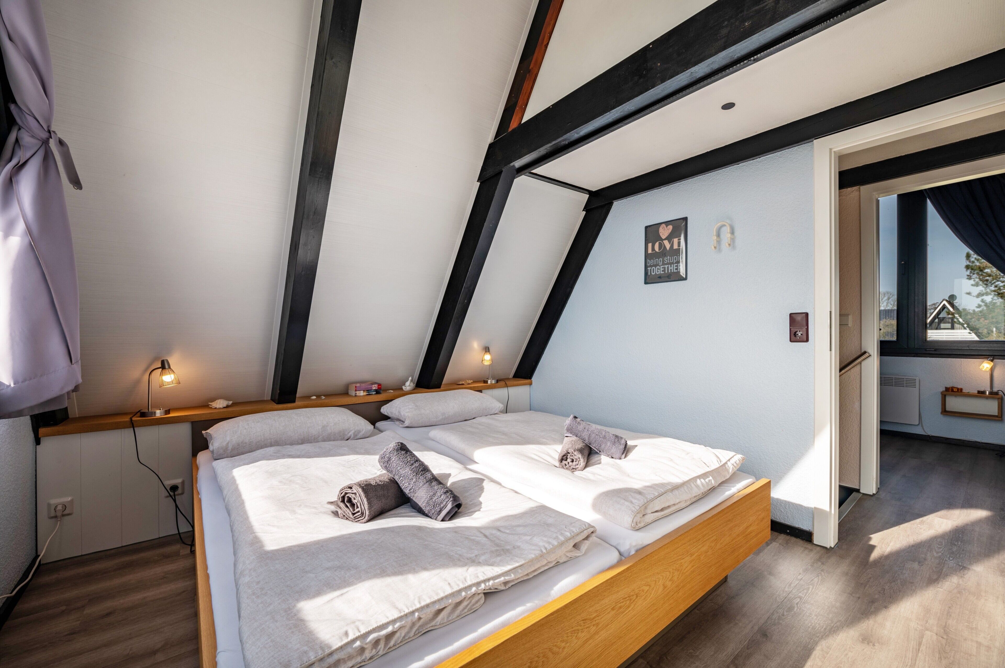 A modern bedroom with a wooden bed, a desk, and a window with curtains.