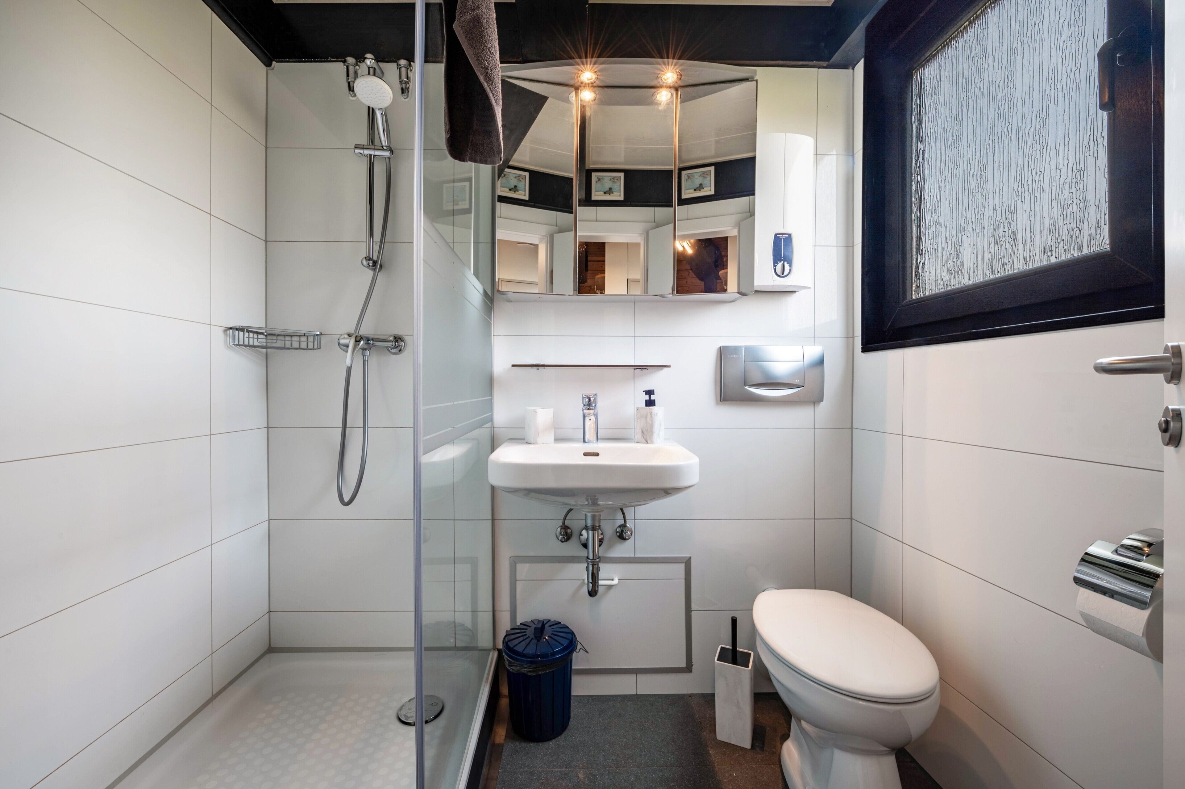 A modern bathroom with a glass shower enclosure, a white sink, a toilet, and a mirror with a decorative frame.