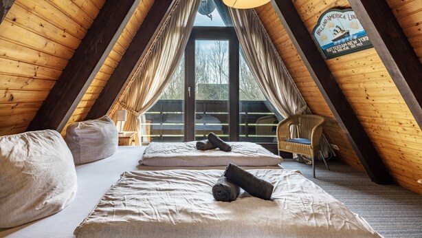 Un dormitorio de ático acogedor con vigas de madera, un ventanal y vistas al exterior.