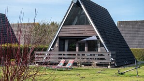 Un edificio de forma triangular con techo inclinado, una terraza con dos sillones y una antena parabólica en el techo.
