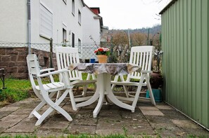 A patio with white chairs and a table, a potted plant, and a green shed. - Holiday Home 'Haus Unterm Räuschenberg' with Mountain View, Private Terrace & Wi-Fi (Höxter)
