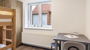 A room with a bunk bed, a table with a chair, a window with a view of a building, and a radiator. - Haus Fuldablick 'Room 3' with Shared Garden and Wi-Fi (Rotenburg an der Fulda)
