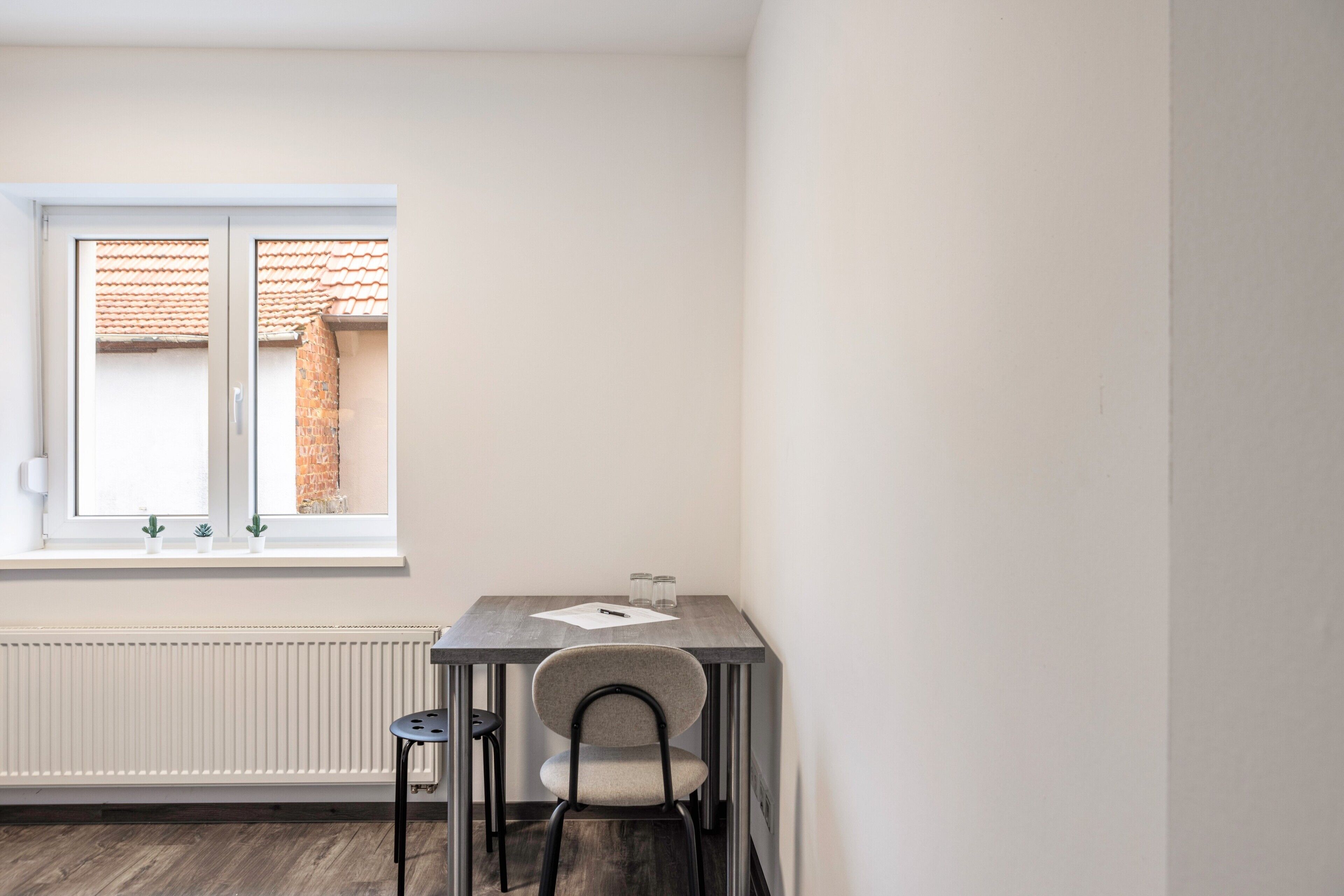Ein kleiner Raum mit Fenster, Heizkörper, Tisch und Stuhl.