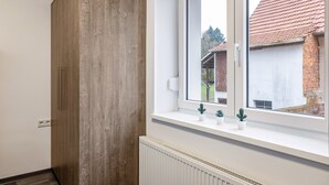 A room with a wooden wardrobe, a window with a view of a brick house, and a radiator below the window. - Haus Fuldablick 'Room 3' with Shared Garden and Wi-Fi (Rotenburg an der Fulda)