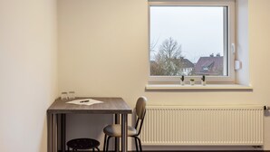 A small room with a table, a chair, a radiator, and a window with a view of buildings. - Haus Fuldablick 'Room 2' with Shared Garden and Wi-Fi (Rotenburg an der Fulda)
