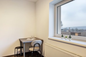 Habitación de esquina con una mesa, una silla, un radiador y una ventana con vistas a edificios.