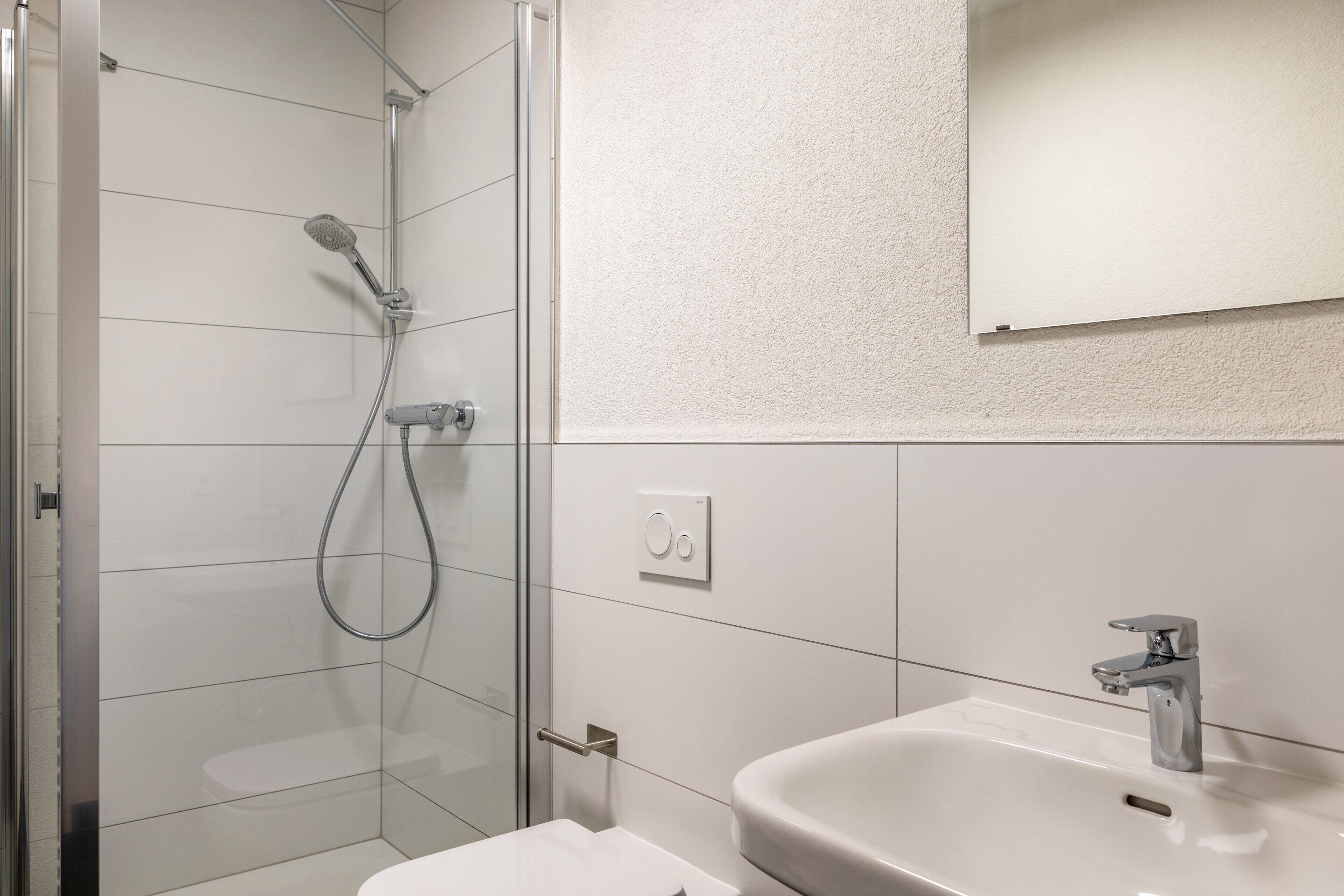 Un baño moderno con cabina de ducha de vidrio, lavamanos blanco y espejo montado en la pared.